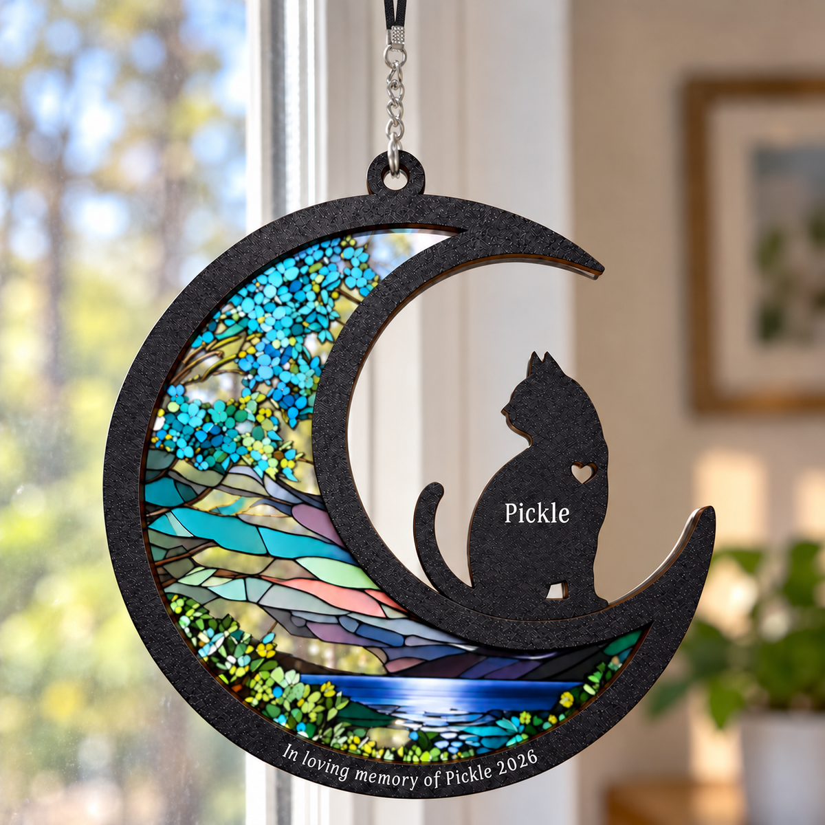 Cat memorial crescent ornament hanging by a window with clear unpainted acrylic and black nylon silver-chain hanger