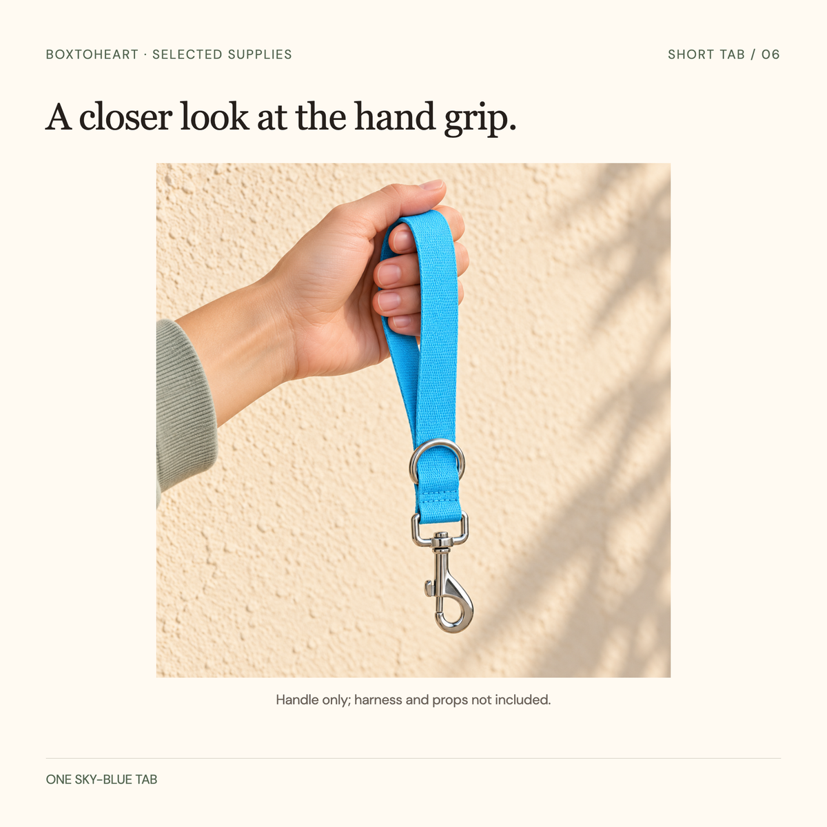 Closeup of an adult hand gripping one sky-blue woven loop, with the whole short tab, silver clip and base D-ring visible against a warm outdoor wall.