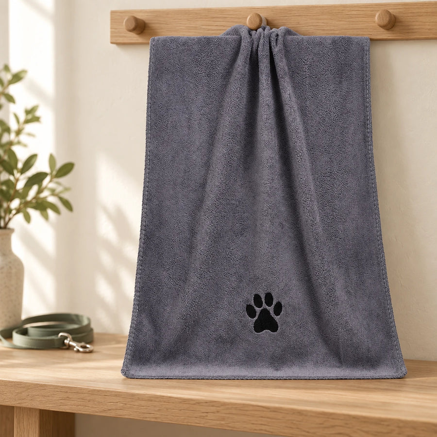 One grey dog towel with a black paw motif hanging from an oak peg in a warm home entryway.