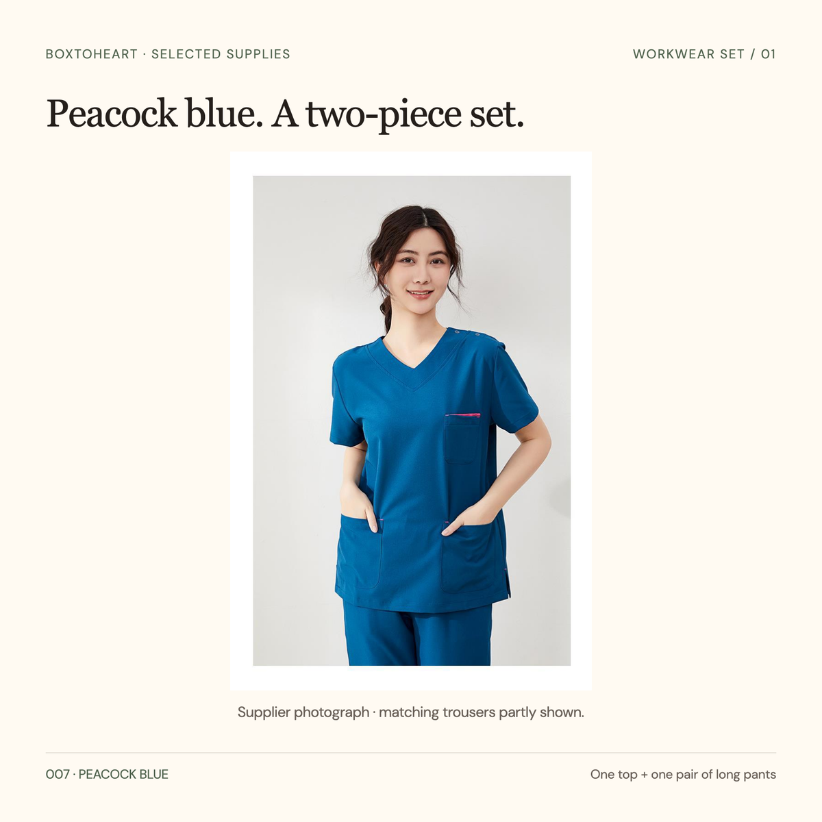 Supplier front photograph of the selected peacock-blue V-neck short-sleeve top with pink chest trim, three front pockets and matching trousers partly visible.